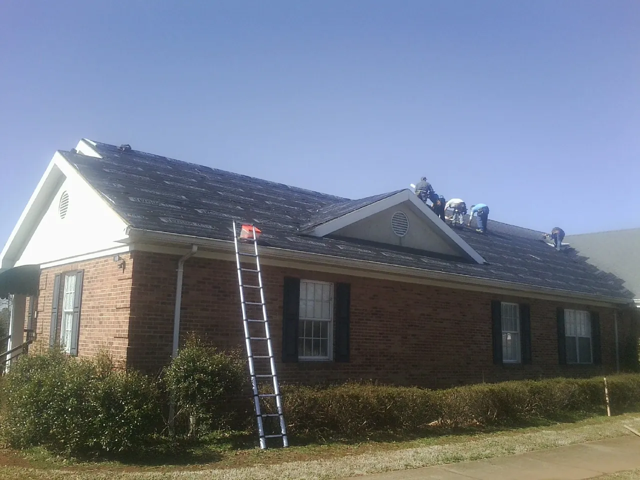 Crew tearing shingles off a brick ranch roof with a ladder set — Emergency Roof Repair work by our crew in East Wareham