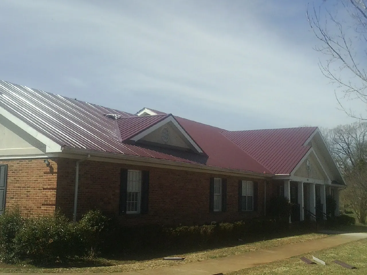 Red metal roof with gabled entries on a long brick building, from a Hail Damage Roof Repair job in East Wareham