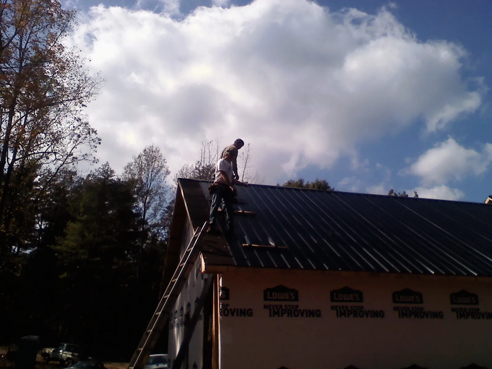 Roofer fastening dark metal panels high against a cloudy sky, from a Roof Inspection job in East Wareham