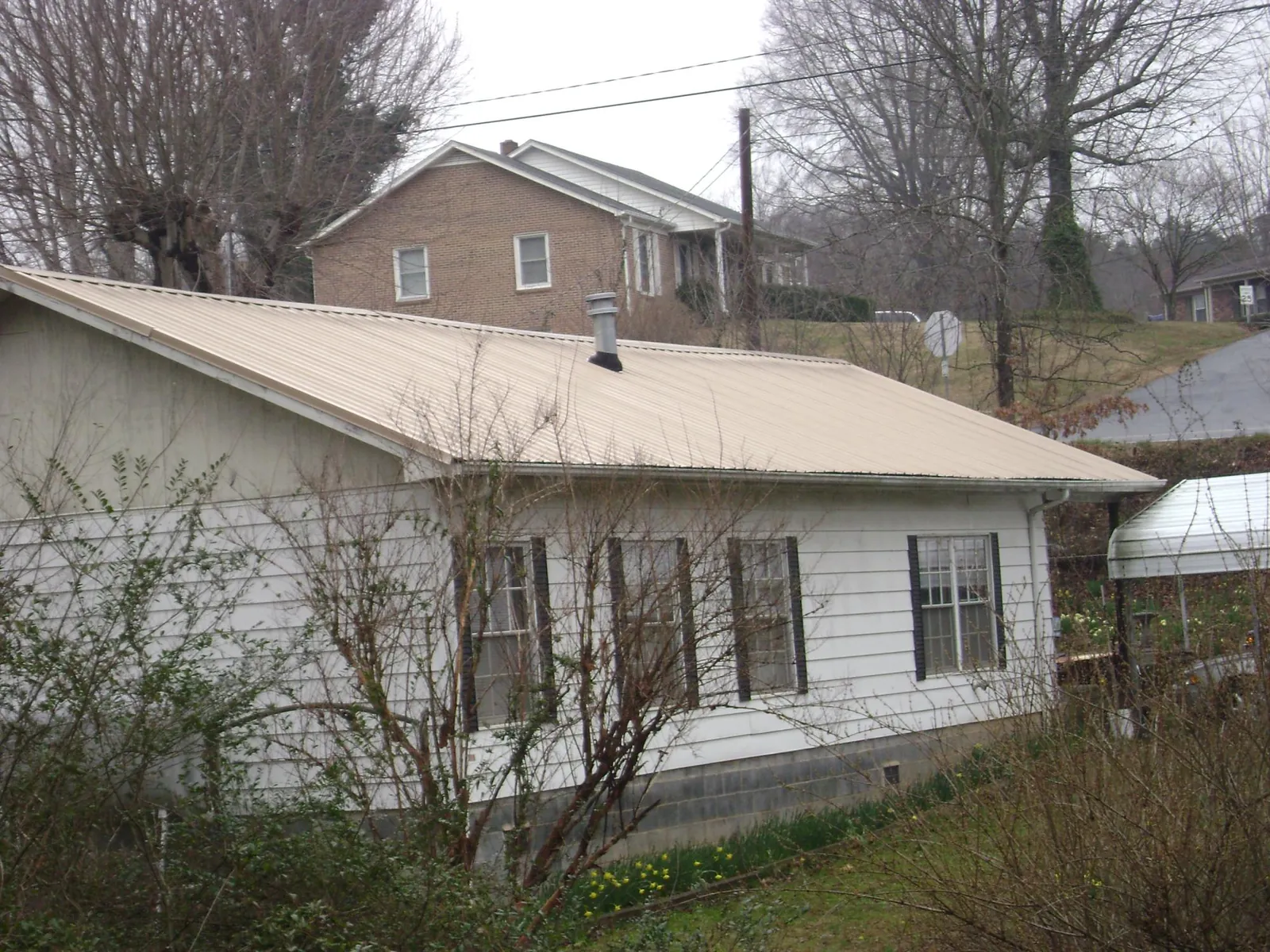 Tan metal roof on a white sided house set into a hillside — Commercial Roofing by Roofing Brothers in East Wareham
